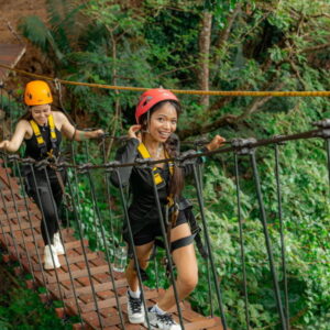 Guests walking a rope bridge in helmets and harnesses