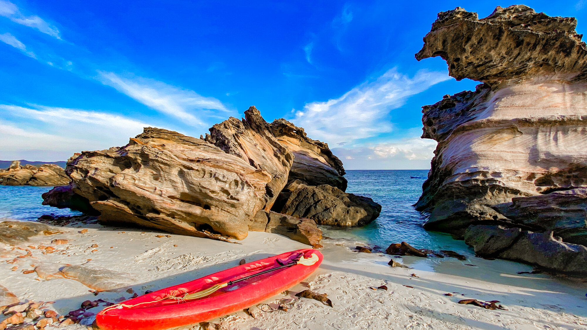 Rock formations and a kayak on a white sand beach
