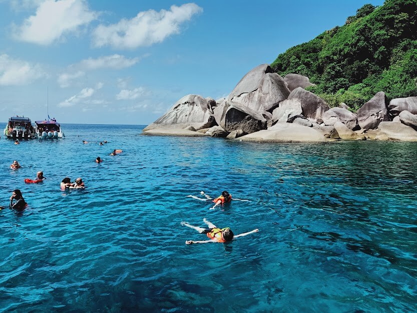 Snorkellers in clear water beside granite boulders in the Similan Islands